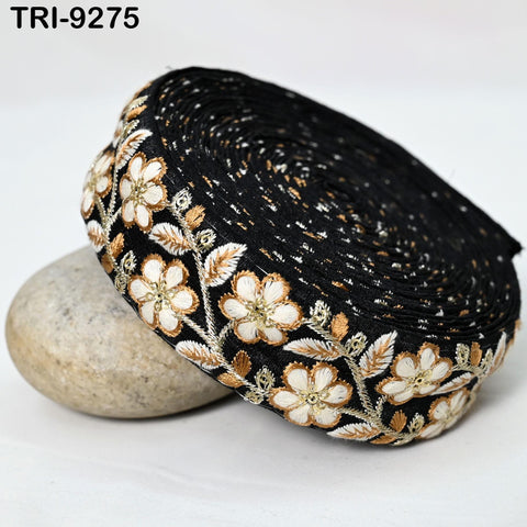 a black and gold embroidered fabric with a floral pattern, resting on a white surface.