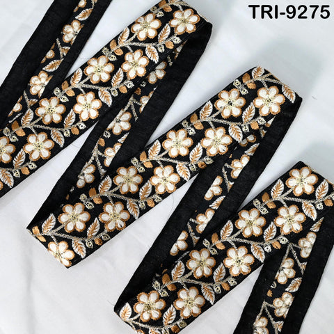 a close-up view of a decorative fabric with a floral pattern in black and gold colors. The fabric appears to be a ribbon or a piece of cloth with a similar design.