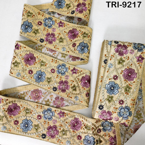 a decorative fabric with a floral pattern in shades of blue, pink, and yellow. The fabric appears to be a decorative trim or border, with a repeating floral design. The fabric is arranged in a way that it covers the entire frame, creating a visually appealing and intricate design.