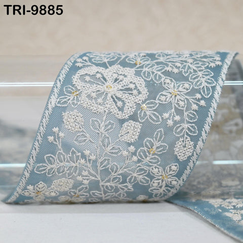 a close-up view of a decorative fabric with intricate white floral patterns and gold accents. The fabric appears to be a piece of lace or a similar type of material, with a blue and white color scheme.