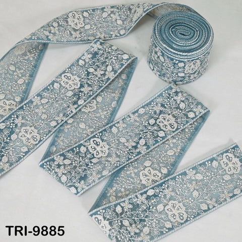 a roll of blue and white floral embroidered ribbon, with the text "TRI-9885" visible.