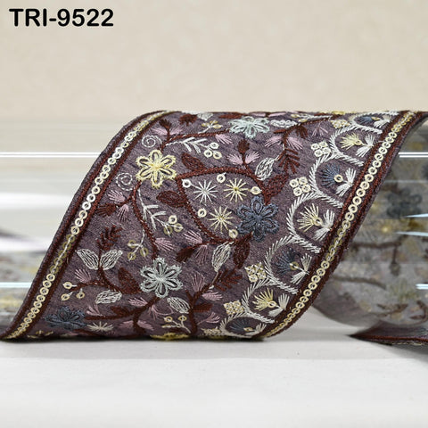 a decorative fabric with a floral pattern, including various shades of purple, white, and gold. The fabric appears to be a ribbon or a piece of cloth with an intricate design.