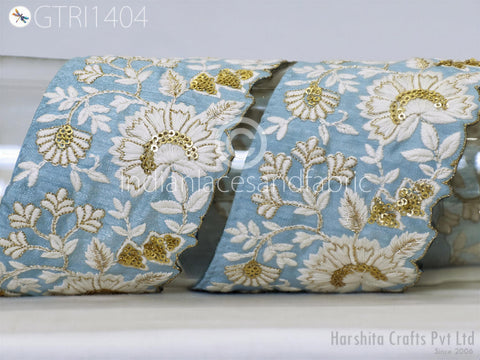 a close-up view of a decorative fabric with a floral pattern in shades of blue and white, adorned with gold sequins and beads.