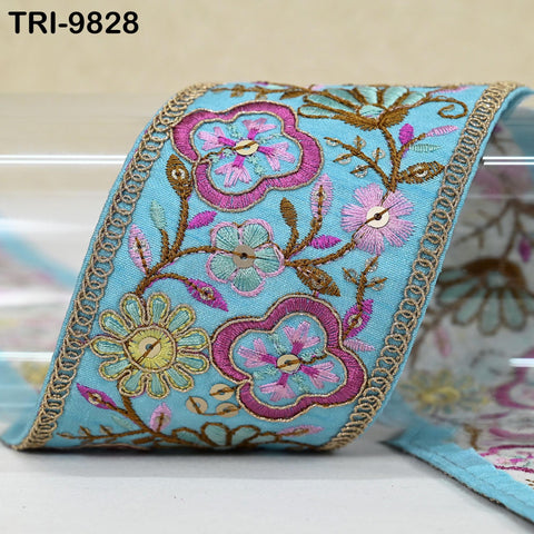a decorative fabric with a floral pattern in shades of blue, pink, and green. The fabric appears to be a ribbon or textile with intricate embroidered designs.