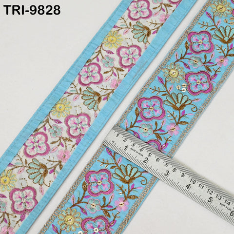 two pieces of fabric with intricate floral embroidery in shades of blue and pink. A ruler is placed on the fabric, indicating the size of the fabric pieces.