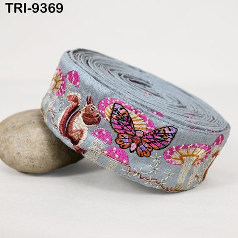 A gray fabric with a butterfly and a squirrel embroidered on it, along with other colorful floral designs.