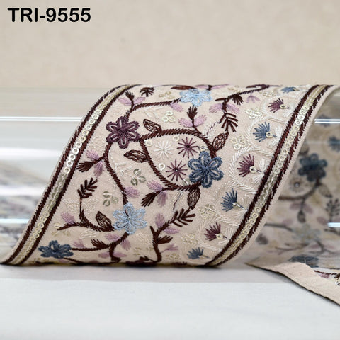 a decorative fabric with a floral pattern, including various shades of blue, purple, and white flowers and leaves. The fabric appears to be a piece of embroidered cloth or a decorative textile.