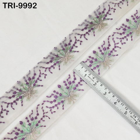 a close-up view of a decorative fabric with a floral pattern, featuring purple and green flowers and leaves. A ruler is placed on the fabric, indicating the size or dimensions of the design.