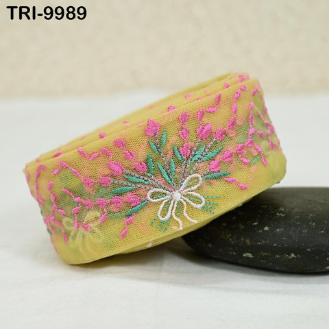 a yellow fabric with pink and green floral embroidery, resting on a black rock.