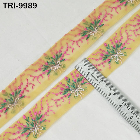 a close-up view of a yellow fabric with a floral pattern, featuring pink and green flowers and leaves. A ruler is placed next to the fabric, indicating its size.