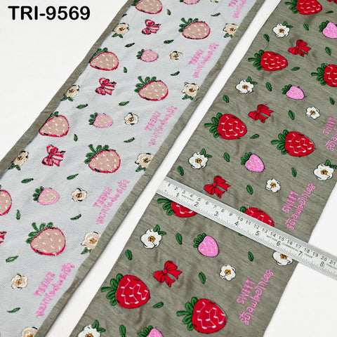 two fabric pieces with a strawberry pattern. The fabric on the left has a white background with pink and green strawberry designs, while the fabric on the right has a gray background with red and green strawberry designs. A ruler is placed between the two fabric pieces, indicating their size.