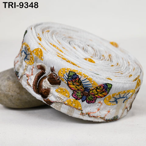 A close-up image of a decorative fabric with a butterfly and a squirrel embroidered on it, along with a rock.