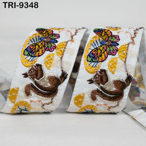 two white fabric pieces with colorful butterfly and bird designs, including a brown squirrel. The butterflies and birds are intricately embroidered with yellow and orange patterns.