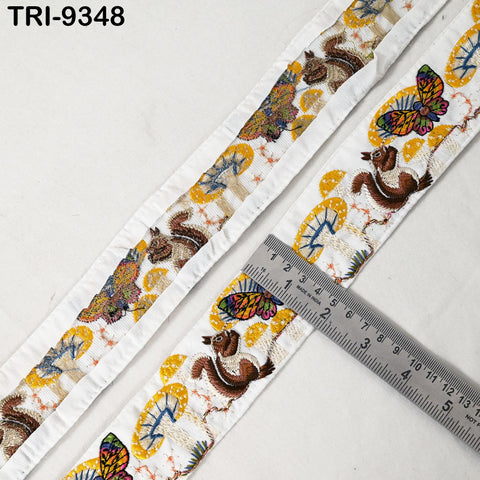 a close-up view of a decorative fabric with a repeating pattern of butterflies and squirrels. A ruler is placed on the fabric, indicating its size.