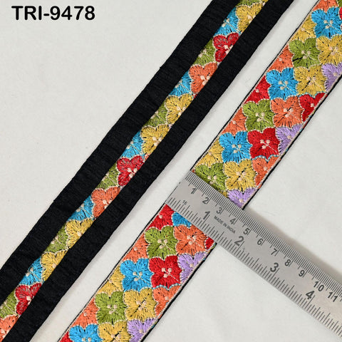 a colorful floral embroidered ribbon with a black border, placed on a white surface. A ruler is placed next to the ribbon, indicating its size.