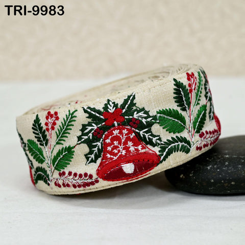 A beige fabric with a red bell and green leaves, along with red berries, is displayed on a white surface.