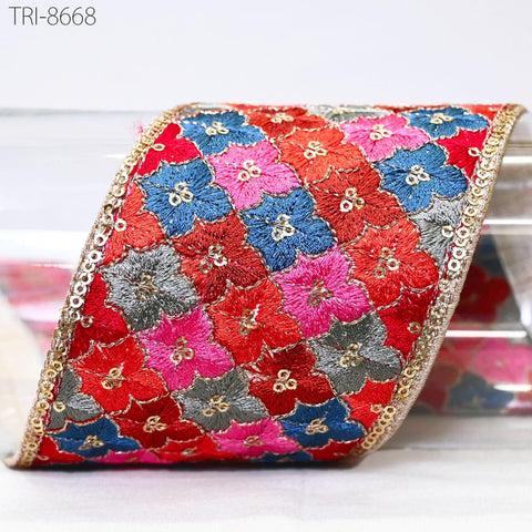 a vibrant, intricately embroidered fabric with a repeating pattern of red, blue, and pink flowers. The fabric is adorned with a gold border, adding a touch of elegance to the overall design. The image showcases the craftsmanship and attention to detail that went into creating this beautiful piece of textile art.