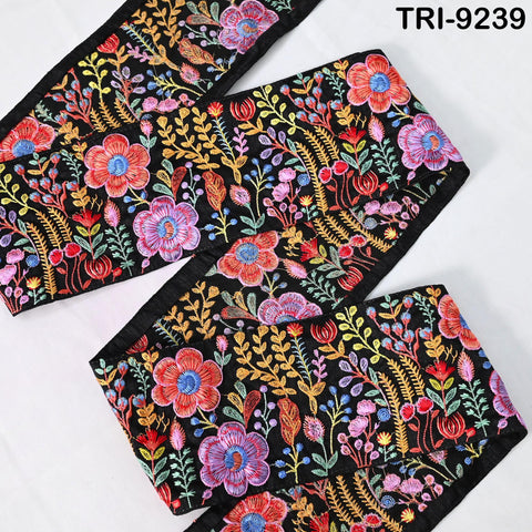 a close-up view of a decorative fabric with a floral pattern in various colors, including red, orange, yellow, and green. The fabric appears to be a black material with intricate embroidered designs.