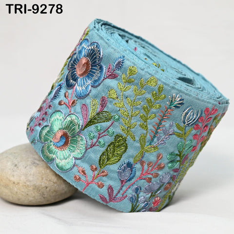A roll of embroidered fabric with a floral pattern, featuring a variety of colorful flowers and leaves.