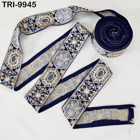 a roll of decorative fabric with a floral pattern in shades of blue and gold. The fabric appears to be a decorative trim or ribbon, and it is placed on a white surface.