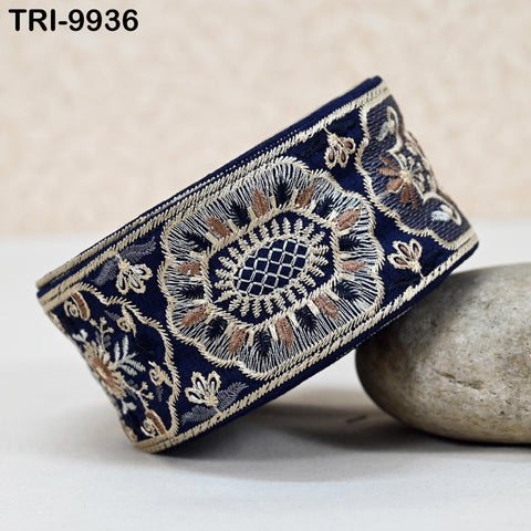 A decorative blue and gold embroidered fabric, possibly a cuff or sleeve, is displayed on a white surface next to a gray rock.