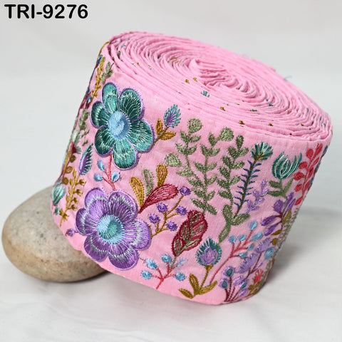 a pink fabric with a floral design, including purple and green flowers, as well as green leaves and stems. The fabric appears to be rolled up and placed on a surface, with a rock visible in the background.
