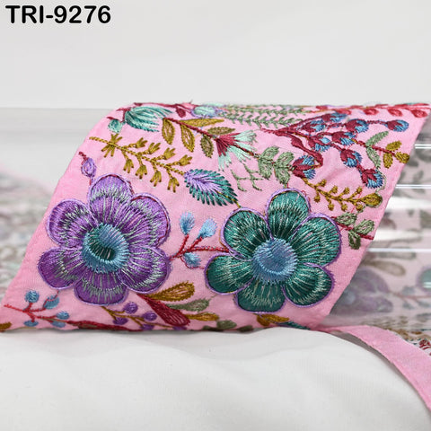 a close-up view of a pink fabric adorned with intricate floral embroidery in shades of green, purple, and blue.