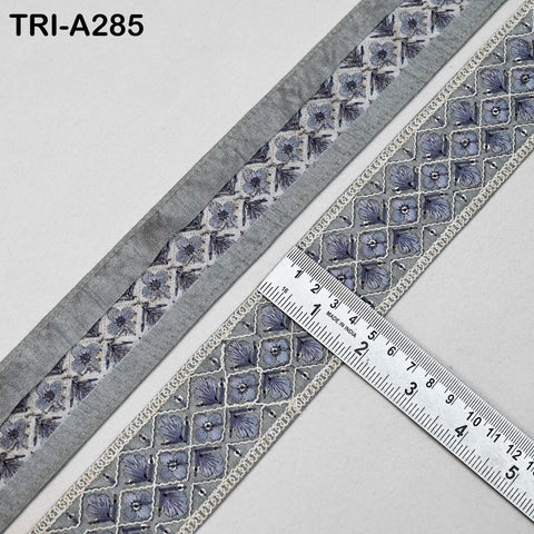 a close-up view of a decorative gray and white fabric with a repeating pattern of small blue flowers or leaves. A ruler is placed on the fabric, indicating the size or dimensions of the pattern.