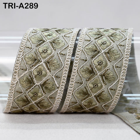 a decorative fabric with a repeating pattern of small flowers or leaves, arranged in a diamond shape. The fabric appears to be a type of lace or ribbon, with a beige or gray color. The pattern is intricate and detailed, creating a visually appealing design.