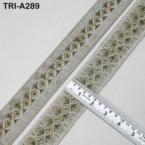 a close-up view of a decorative fabric with a repeating pattern of small, intricate designs. The fabric appears to be made of a material with a metallic or metallic-like appearance, and it is placed on a white surface. A ruler is visible in the image, likely used for measuring the size or dimensions of the fabric.