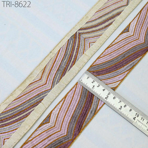 a close-up view of a decorative fabric with a striped pattern, placed next to a ruler for size comparison.