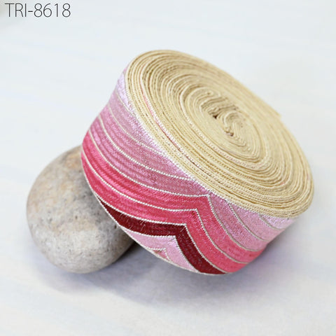 a pink and beige decorative ribbon with a zigzag pattern, resting on a white surface next to a small gray rock.