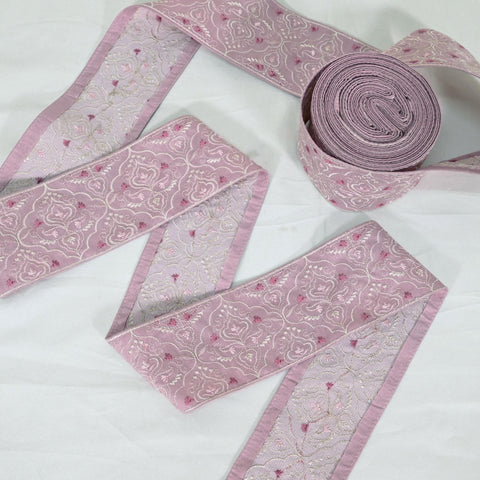 a collection of pink and white floral embroidered fabric pieces, including a large roll of fabric with a floral pattern and smaller pieces of fabric with similar patterns.