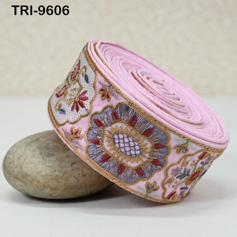 A pink and gold embroidered fabric with a floral design is shown, resting on a rock.