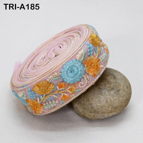 A pink and blue floral embroidered ribbon is rolled up and resting on a rock.