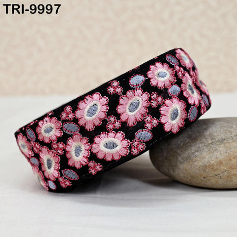 A black and pink floral embroidered headband is placed on a gray rock.