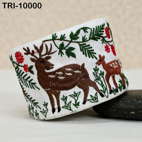 a white fabric with a decorative embroidered design of deer and green foliage.
