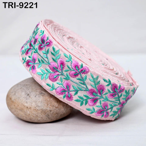 A pink and green floral embroidered fabric is displayed on a white surface, with a rock placed next to it.