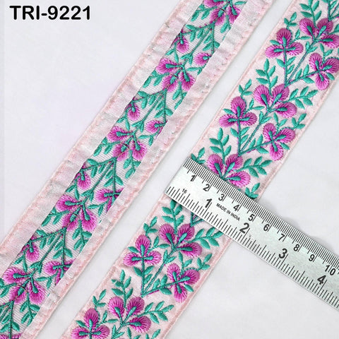 a close-up view of a decorative ribbon with a floral pattern in shades of pink and green. A ruler is placed on the ribbon, indicating its size.