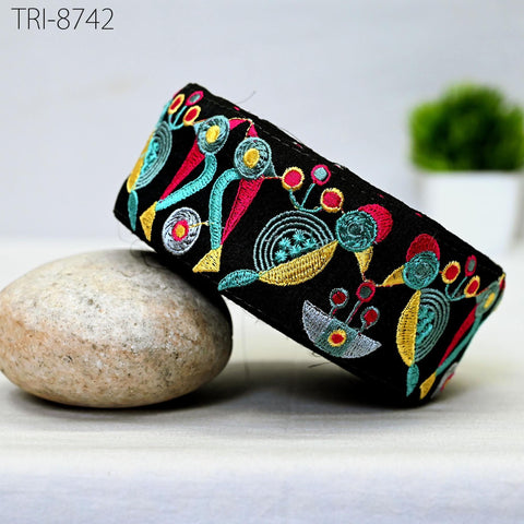 a black, embroidered headband with a colorful floral design, resting on a rock.