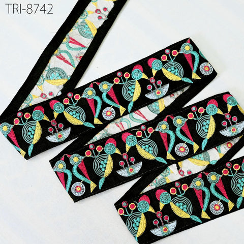a colorful, patterned fabric with a repeating design of various shapes and colors, including flowers, leaves, and geometric patterns. The fabric appears to be a decorative piece, possibly used for clothing or accessories.