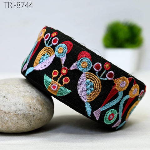 a black headband with a colorful, embroidered design on it, placed on a white surface next to a rock.