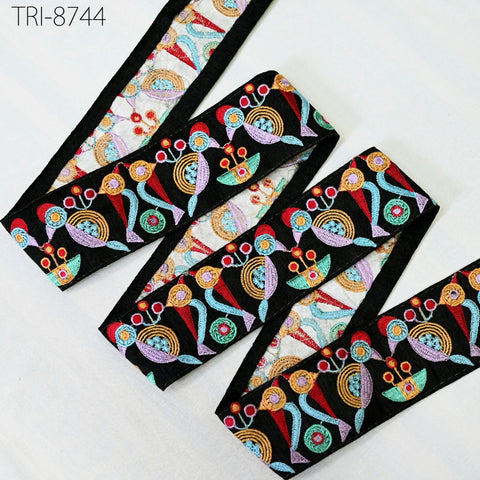 a colorful, patterned fabric with a repeating design of flowers and leaves in various colors, including red, blue, green, and yellow. The fabric appears to be a decorative textile, possibly used for clothing or home decor.