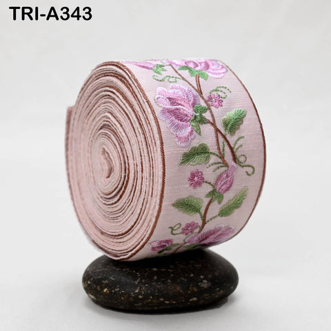 A pink fabric with a floral embroidered design is rolled up and placed on a small rock.