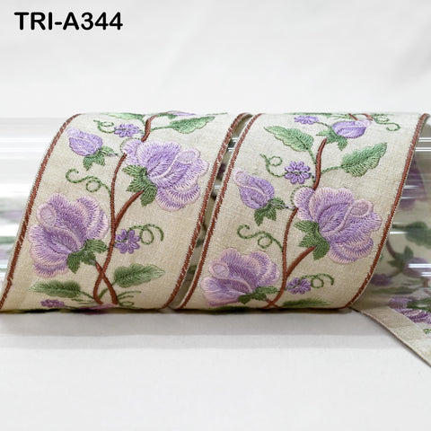 a close-up view of a decorative fabric with a floral pattern, including purple flowers and green leaves. The fabric appears to be a beige color, and the floral design is intricate and detailed.