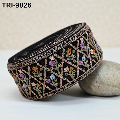 A close-up image of a decorative black fabric with a floral pattern, featuring a variety of colors including pink, purple, and green. The fabric is placed on a white surface, with a rock visible in the background.
