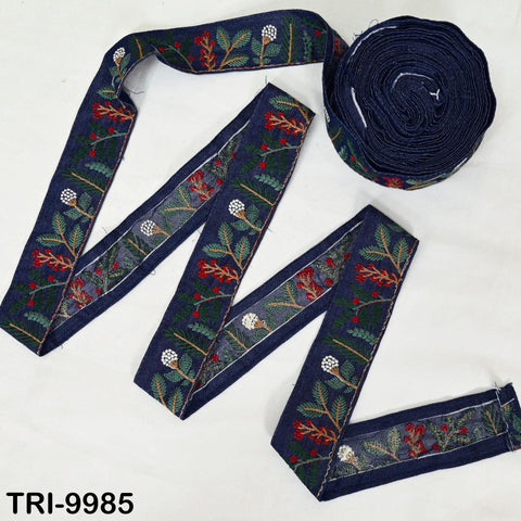 a spool of embroidered fabric with a floral pattern, along with a piece of fabric that appears to be a ribbon or a similar decorative item.