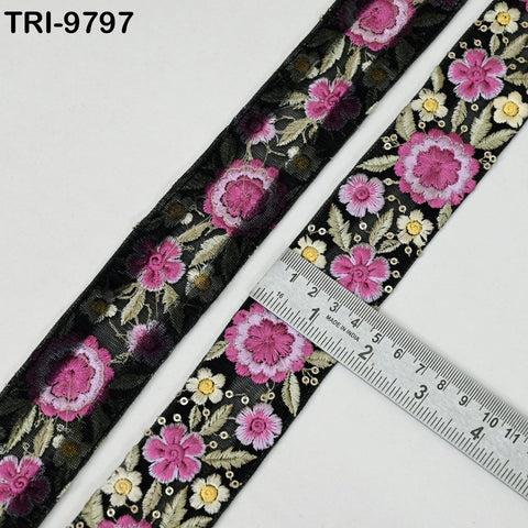 a close-up view of a decorative fabric with a floral pattern, featuring pink and white flowers on a black background. A ruler is placed on the fabric, indicating its size.
