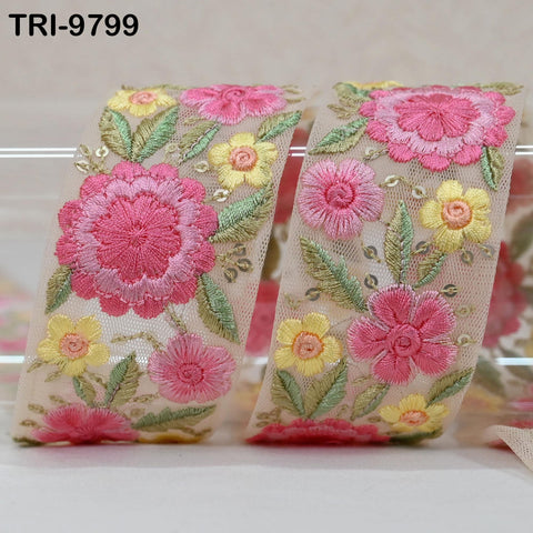 a decorative fabric with a floral pattern, including pink and yellow flowers, green leaves, and a pink flower. The fabric appears to be a ribbon or a piece of lace, with the floral design being the main focus.