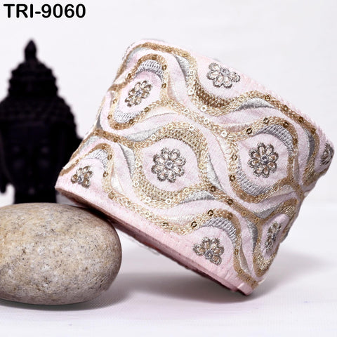 a pink and gold embroidered bracelet with a floral pattern, placed on a white surface next to a gray rock.